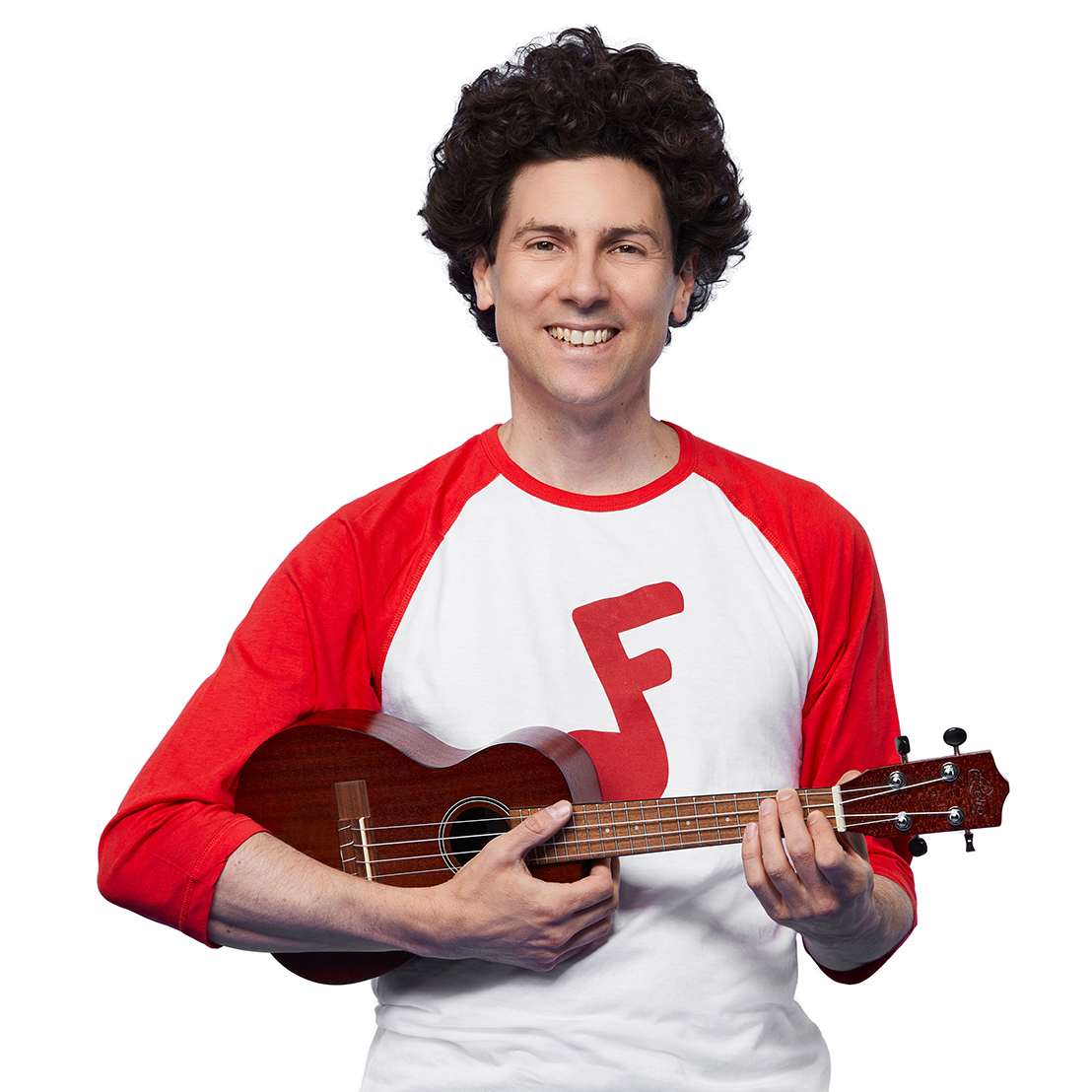 Jeremy Fisher, a white man with curly brown hair, grins at the camera. He is holding a ukulele and wearing a red and white shirt with a red Jeremy and Jazzy logo