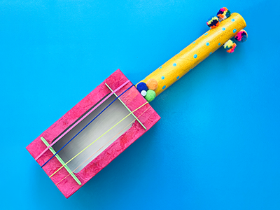 A brightly-coloured ukulele made out of a tissue box and paper towel roll