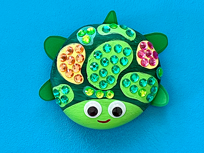 A rock painted to look like a turtle, with googly eyes and gems.